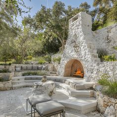 an outdoor fireplace and seating area with stone walls, steps and trees in the background