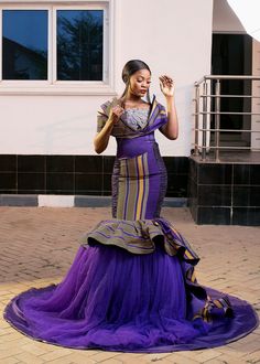 a woman in a purple dress standing on a brick floor next to a white building