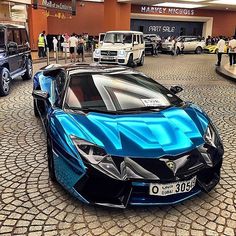 a blue sports car parked in front of a building with people standing around and looking at it