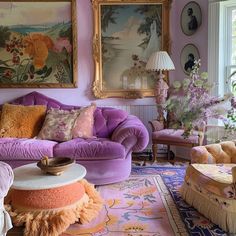 a living room filled with lots of purple furniture and paintings on the wall above it