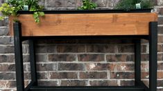 a wooden planter with plants growing out of it on top of a brick wall