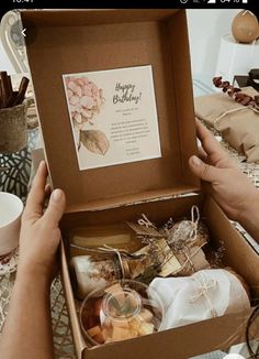 a person holding an open gift box filled with food and drinks on a table next to other items