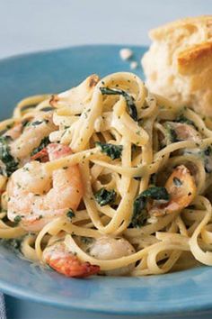 pasta with shrimp, spinach and garlic bread on a blue plate next to a biscuit