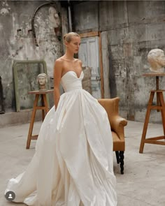 a woman in a white wedding dress standing next to a chair