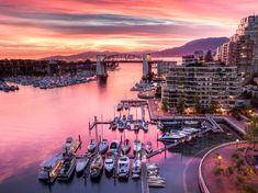 boats are docked in the water at sunset near a city and bridge with mountains in the background