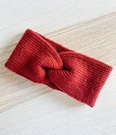 a red knitted headband with a knot on it sitting on top of a wooden table