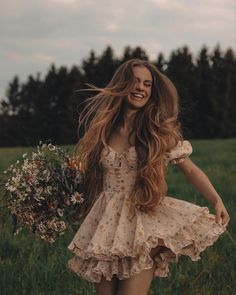 a woman with long brown hair is walking through the grass holding a bouquet of flowers