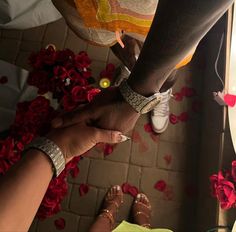 two people holding hands with red flowers on the ground in front of them and one person wearing white shoes