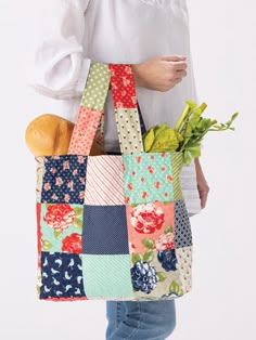 a woman holding a multicolored patchwork tote bag with fruit and vegetables in it