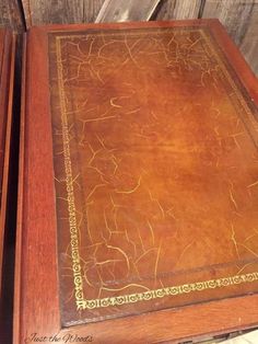 two wooden tables with brown leather coverings on top of each other and one has gold trim around the edges