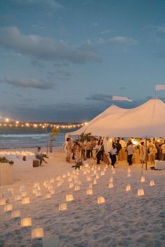 a group of people standing on top of a beach next to a white tent covered in paper lanterns