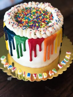 a birthday cake decorated with sprinkles and colorful icing on a gold plate