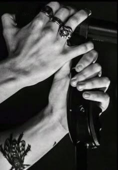 two hands holding onto each other with tattoos on their arm and wrist, while the other hand holds an object