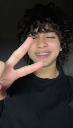 a young man making the peace sign with his fingers in front of him and wearing a black t - shirt