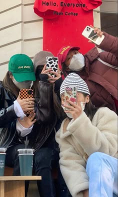 four people sitting on a bench with masks covering their faces and holding coffee cups in front of a building