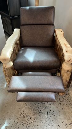 a brown leather reclining chair and footstool in front of a black cabinet