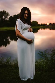 a pregnant woman standing in front of a body of water