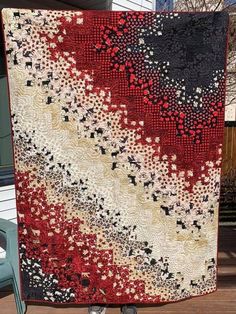 a red, white and black quilt hanging on a wall in front of a house