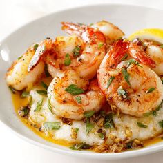 a white bowl filled with shrimp and grits on top of a table next to a lemon wedge