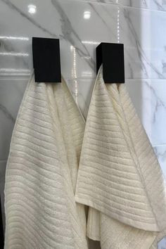 two white towels hanging on the side of a bathroom wall next to a black towel rack