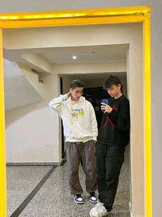 two young men standing in front of a mirror looking at their cell phones and taking a selfie