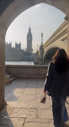 a woman is walking down the sidewalk in front of big ben and the river thames