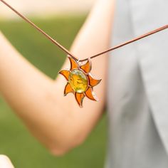 an orange glass sunburst hanging from a string on a person's arm