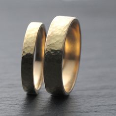 two gold wedding rings sitting on top of a black table next to each other,