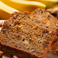 three slices of banana bread sitting on top of a wooden cutting board next to bananas