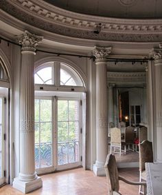 an ornate room with large arched windows and white chairs in the center, on hard wood flooring