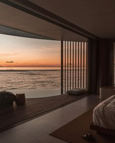 a bed sitting next to a large window on top of a wooden floor near the ocean