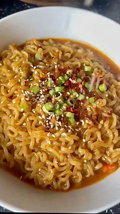 a white bowl filled with noodle soup on top of a table next to a spoon