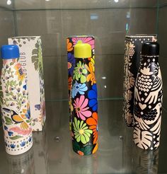 three different colored vases sitting on top of a glass shelf next to each other