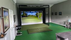 an indoor golf simulator is set up in a room with green carpet and white walls