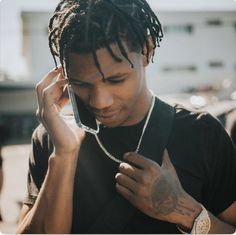 a man with dreadlocks talks on his cell phone while wearing a black t - shirt