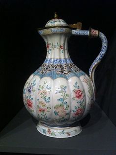 a white vase with blue and pink flowers on it's sides is sitting on a black surface