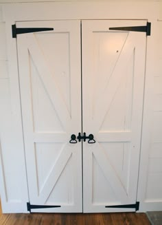 two white barn doors with black hardware on the top and bottom, in front of a wood floor