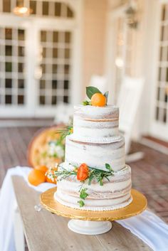 a wedding cake sitting on top of a wooden table next to an orange and white flower arrangement