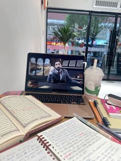 an open laptop computer sitting on top of a wooden table next to books and notebooks