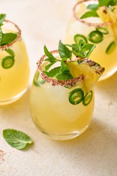 three glasses filled with drinks and garnished with green leaves