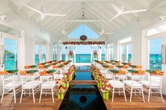 an indoor dining area with white chairs and tables set up next to a pool in front of the ocean