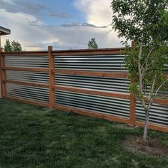 a wooden fence with metal slats on the top and bottom, next to a small tree