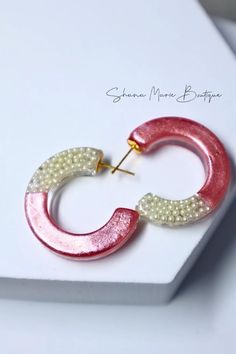 a pair of pink and white hoop earrings with pearls on them sitting on top of a box