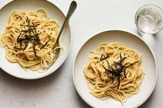 two white bowls filled with pasta and topped with seaweed next to a glass of water