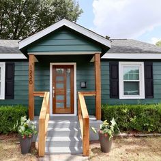 a green house with black shutters and wooden steps leading up to the front door