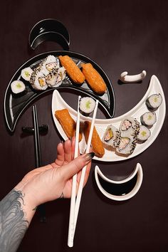 a person holding chopsticks and sushi in front of an assortment of food