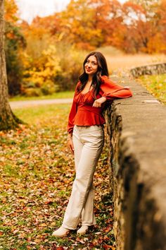 a woman leaning against a stone wall in the fall