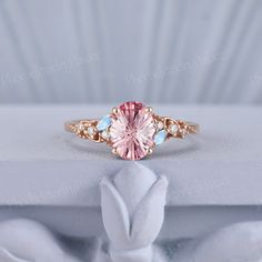 a pink and blue ring sitting on top of a white cloth covered box with flowers