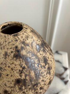 a brown and black vase sitting on top of a marble table next to a white wall