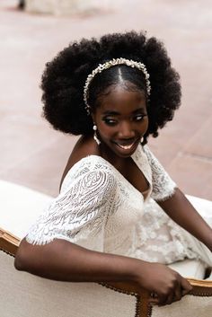 a woman with an afro sitting on a chair smiling at the camera while wearing a white dress